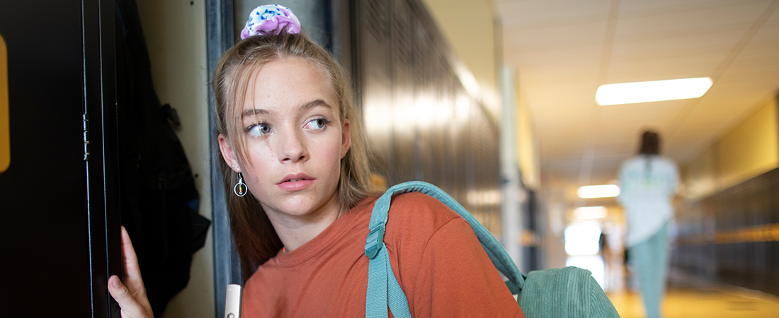 a teen standing at her school locker, looking into the hallway